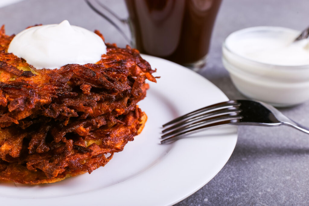 Hash brown and sour cream on a plate against gray stone background, well fried.